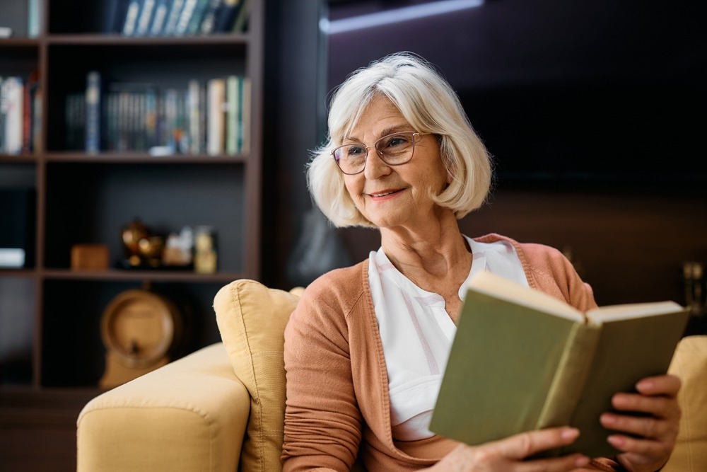 Happy,Senior,Woman,Enjoying,While,Reading,Book,In,Living,Room